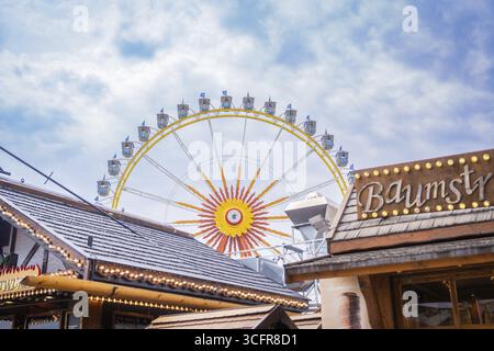 Grande roue derrière des bâtiments en bois, dans un ciel lumineux et nuageux, Olympiapark, Munich, Allemagne Banque D'Images