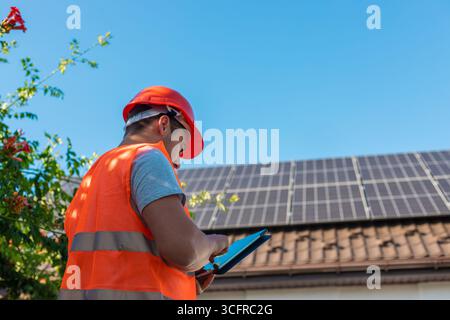 Ingénieur avec tablette inspectant les panneaux solaires sur le toit. Banque D'Images