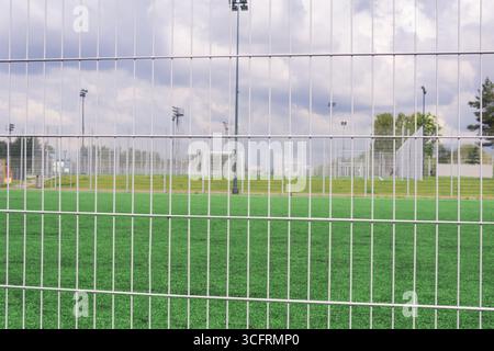 Terrains de sport et terrains de football derrière une clôture métallique avec de l'herbe verte et un ciel bleu Banque D'Images