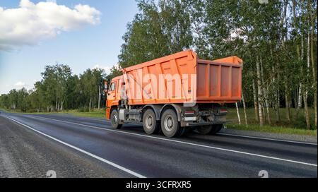 Camion benne basculante sur la route. Du matériel de construction circule sur l'autoroute. Une voiture avec une carrosserie pour transporter des matériaux en vrac. Vue arrière du camion Orange. Banque D'Images