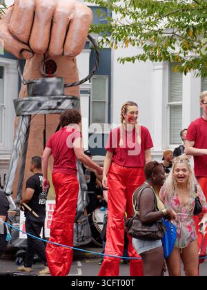 Des gens en rouge sur pilotis, y compris une femme en queue de cochon avec le visage partiellement peint pendant le carnaval de Notting Hill, Londres. Angleterre 25 août 2025 Banque D'Images