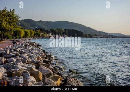 Les gens se promènent le long d'une promenade au bord de l'eau à côté des rochers brise-lames sur la mer de Marmara. Karamürsel, Kocaeli, Türkiye – 23 août 2025. Banque D'Images
