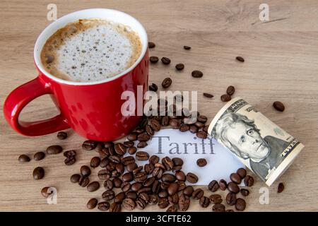 Une tasse de café, des grains de café, le mot imprimé tarif et un rouleau de billets en dollars américains sur une table. Un concept de tarif du café. Banque D'Images
