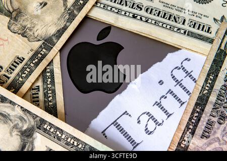 Londres. Royaume-Uni- 20 août. 2025. Le logo de la société Apple, le mot imprimé Tarif entouré de billets en dollars des États-Unis. Un concept de taxe tarifaire électronique à la consommation. Banque D'Images