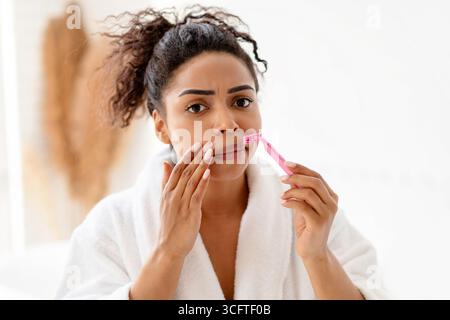Femme se raser les moustaches enlever les cheveux de lèvre supérieure du visage dans la salle de bains Banque D'Images