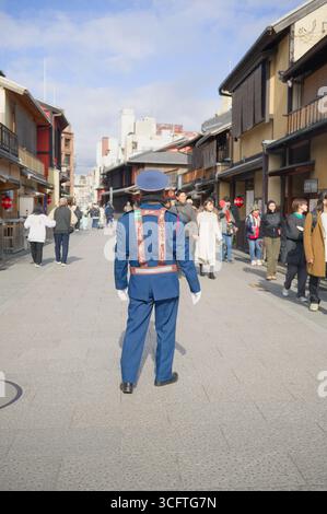 Un officier en uniforme se tient debout regarder les gens marcher le long d'une rue historique par une journée ensoleillée d'hiver Banque D'Images