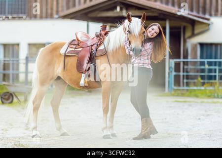 Cowgirl avec cheval Haflinger dans le tack occidental à l'extérieur de l'écurie Banque D'Images