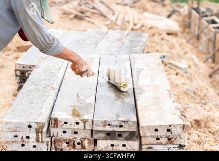 Travailleur appliquant de l'huile ou un revêtement protecteur sur des panneaux de construction en acier, gros plan de la main avec le rouleau Banque D'Images