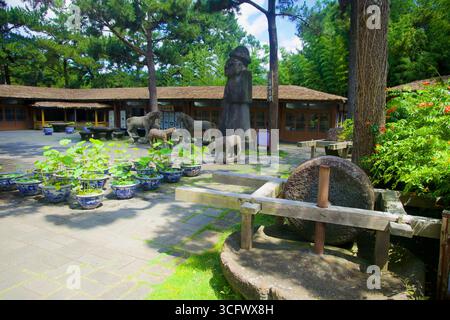Vue panoramique sur la cour du village folklorique de Hallim Park sur l'île de Jeju, avec du lotus en pot, une meule en pierre, une statue de dol hareubang et un cheval sculpté Banque D'Images