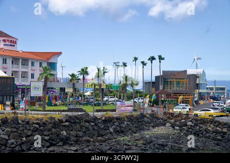 Des boutiques, des cafés et un dépanneur font face aux pelouses du front de mer au port de Panpo, avec des rangées de palmiers et de petites éoliennes visibles derrière le bui Banque D'Images