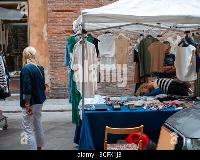 Cremona, Italie- 23 août 2025 marché extérieur des vêtements Stall dans une place italienne exposant des vêtements à la mode pour les acheteurs au milieu de l'historique A. Banque D'Images