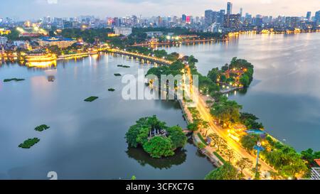 Vue aérienne de la route traversant l'île Westlake avec rue bordée d'arbres verts, temple situé entre petite oasis. Un beau coucher de soleil dans la capitale Banque D'Images