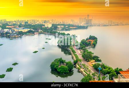 Vue aérienne de la route traversant l'île Westlake avec rue bordée d'arbres verts, temple situé entre petite oasis. Un beau coucher de soleil dans la capitale Banque D'Images