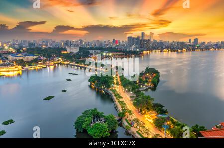 Vue aérienne de la route traversant l'île Westlake avec rue bordée d'arbres verts, temple situé entre petite oasis. Un beau coucher de soleil dans la capitale Banque D'Images