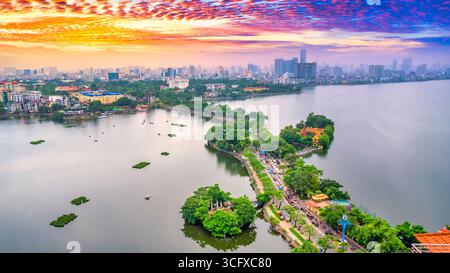 Vue aérienne de la route traversant l'île Westlake avec rue bordée d'arbres verts, temple situé entre petite oasis. Un beau coucher de soleil dans la capitale Banque D'Images