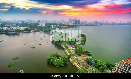 Vue aérienne de la route traversant l'île Westlake avec rue bordée d'arbres verts, temple situé entre petite oasis. Un beau coucher de soleil dans la capitale Banque D'Images