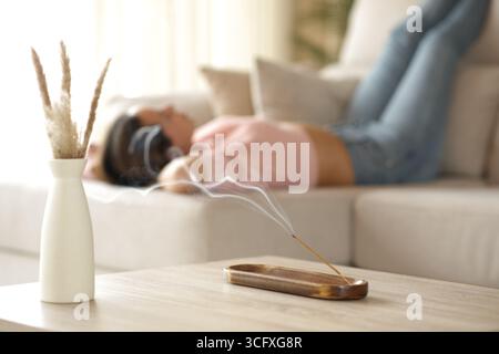 Gros plan d'une femme se relaxant allongée sur un canapé avec un bâton d'encens brûlant au premier plan Banque D'Images