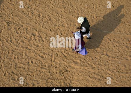Vue aérienne de deux personnes marchant sur le sol sablonneux, projetant de longues ombres dans la lumière chaude du désert, Pushkar, Rajasthan, Inde. Banque D'Images