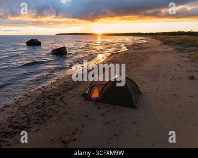 Une tente illuminée sur une plage de sable estonienne lors d'un spectaculaire coucher de soleil doré sur la magnifique mer Baltique. Banque D'Images