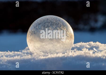 Bulle de savon gelée sur la neige, magie hivernale de bulle de savon gelée avec de beaux cristaux de glace dans une sphère parfaite sur la neige avec un fond flou Banque D'Images