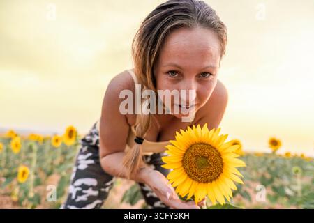 Jeune femme montrant un tournesol dans un champ de tournesols au coucher du soleil Banque D'Images