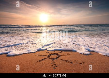 Lever de soleil coloré sur la plage au-dessus de l'horizon de la mer et le soleil dessinant sur le sable Banque D'Images