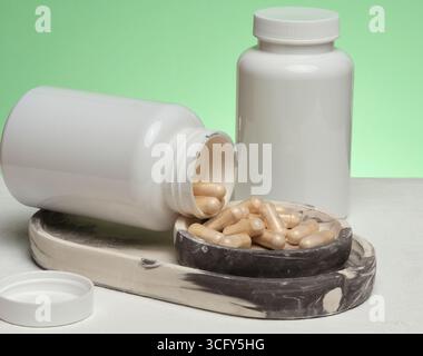 Deux bocaux en plastique blanc, dont l'un est renversé et les capsules débordent, sont placés sur un support en marbre. Banque D'Images