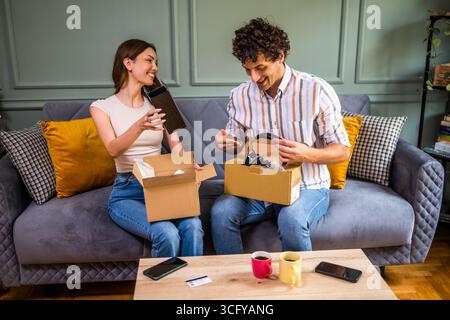 Couple adulte déballage leurs colis livrés à domicile. Ils montrent de nouveaux produits les uns aux autres. Banque D'Images