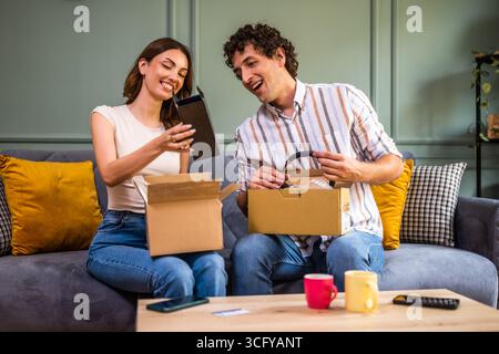 Couple adulte déballage leurs colis livrés à domicile. Ils montrent de nouveaux produits les uns aux autres. Banque D'Images