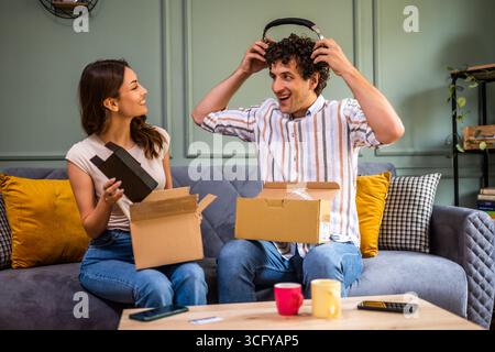 Couple adulte déballage leurs colis livrés à domicile. Ils montrent de nouveaux produits les uns aux autres. Banque D'Images