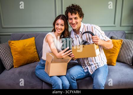 Couple adulte déballage leurs colis livrés à domicile. Ils prennent selfie avec de nouveaux objets. Banque D'Images