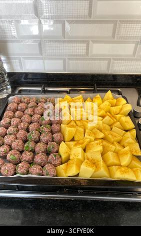 Boulettes de viande crues et cubes de pommes de terre assaisonnés sur un plateau avant de cuire dans un cadre de cuisine maison. Photo mobile Banque D'Images