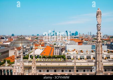 Milan, Italie - 21 juin 2025 : depuis le toit du Duomo de Milan, une statue de marbre s'élève au-dessus d'un patchwork de toits et de dômes avec le skyl de la ville Banque D'Images