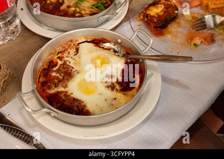 Petit-déjeuner traditionnel shakshuka moyen-oriental composé d'œufs pochés et de grosses sauce tomate et d'ail servis hors de la cuisinière dans une poêle en métal chaude. Banque D'Images