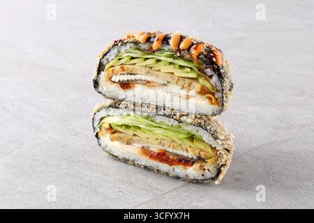 Gros plan d'un sandwich à sushi onigirazu frit rempli d'anguille grillée (unagi), d'avocat, de laitue fraîche et de riz enveloppé dans du nori, garni de m épicé Banque D'Images