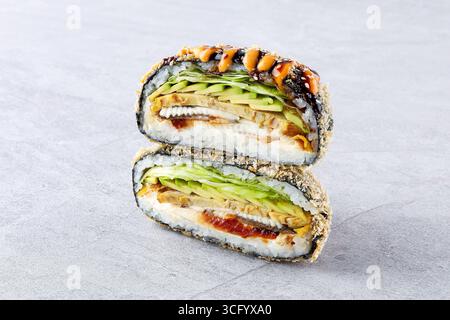 Gros plan d'un sandwich à sushi onigirazu frit rempli d'anguille grillée (unagi), d'avocat, de laitue fraîche et de riz enveloppé dans du nori, garni de m épicé Banque D'Images