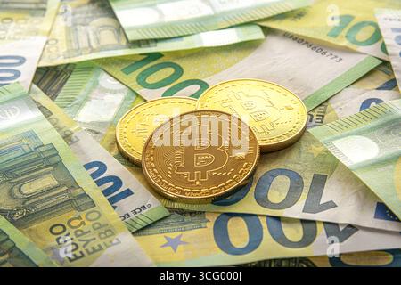 Pièces Golden Bitcoin reposant sur une pile dispersée de billets de 100 euros. Banque D'Images