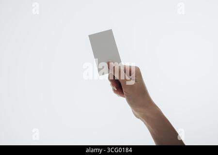 Une main tenant une carte de visite vierge et ordinaire sur un fond blanc propre. Image conceptuelle pour l'identité, la présentation et le professionnalisme. Minima Banque D'Images