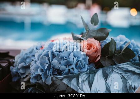 Gros plan d'un bouquet orné d'hortensias bleues et d'une rose rose aux feuilles d'eucalyptus, sur fond flou au bord de la piscine. Capture l'essence Banque D'Images