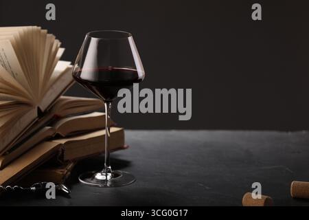 Vin rouge en verre et livres sur table texturée grise sur fond sombre, gros plan. Espace pour le texte Banque D'Images