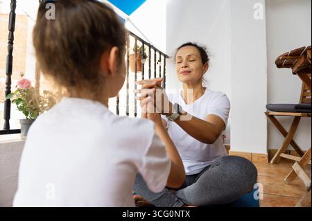 Un parent et un enfant pratiquent le yoga et la pleine conscience sur un balcon ensoleillé, mettant l'accent sur la connexion familiale, la forme physique et la détente dans un envi serein Banque D'Images