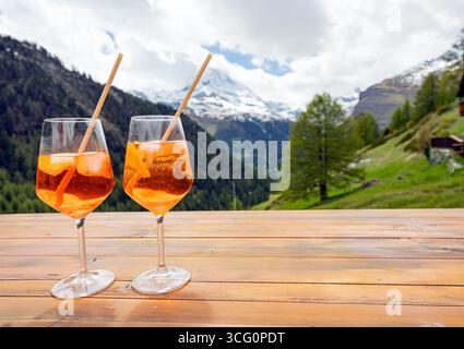 Deux verres de cocktails orange sont assis sur une table en bois, surplombant un paysage montagneux magnifique. Les boissons vibrantes et le décor naturel créent un per Banque D'Images