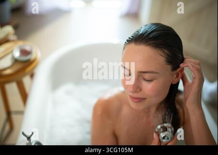 Jeune femme détendue appréciant l'auto-soin et le lavage des cheveux dans la baignoire. Banque D'Images