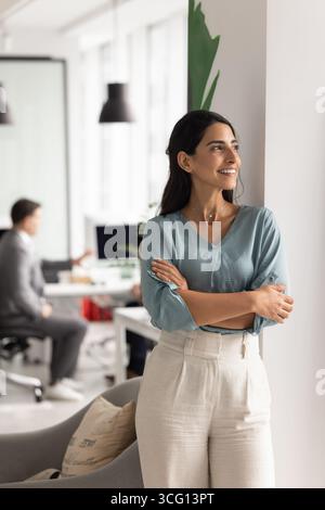 Femme d'affaires se tient dans le bureau regarde dans la distance avec le sourire satisfait Banque D'Images