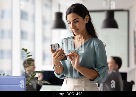 Jeune employée des années 30 utilisant un smartphone sur le lieu de travail Banque D'Images