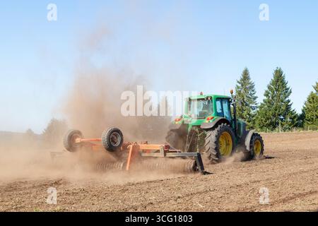 Agriculteur utilisant un rouleau broyeur ou une herse motorisée et un tracteur John Deere sur une terre hivernée préparant le sol ou la nouvelle récolte au début du printemps Banque D'Images