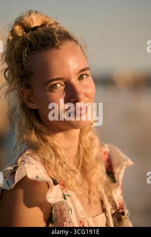 Femme blonde souriante pendant l'heure dorée à la plage Banque D'Images