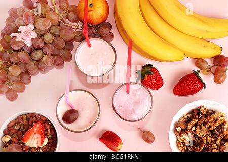 Smoothies à la fraise et à la banane, granola, baies fraîches, bananes et raisins sur un fond rose ensoleillé. Le concept de nourriture saine et naturelle. Usefu Banque D'Images