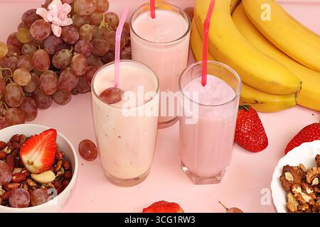 Smoothies à la fraise et à la banane, granola, baies fraîches, bananes et raisins sur un fond rose ensoleillé. Le concept de nourriture saine et naturelle. Usefu Banque D'Images