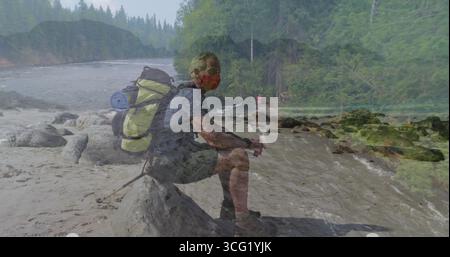 Randonneur assis portant un masque rouge sur une bûche tombée près de la rivière qui coule, portant un sac à dos avec coussin roulé Banque D'Images
